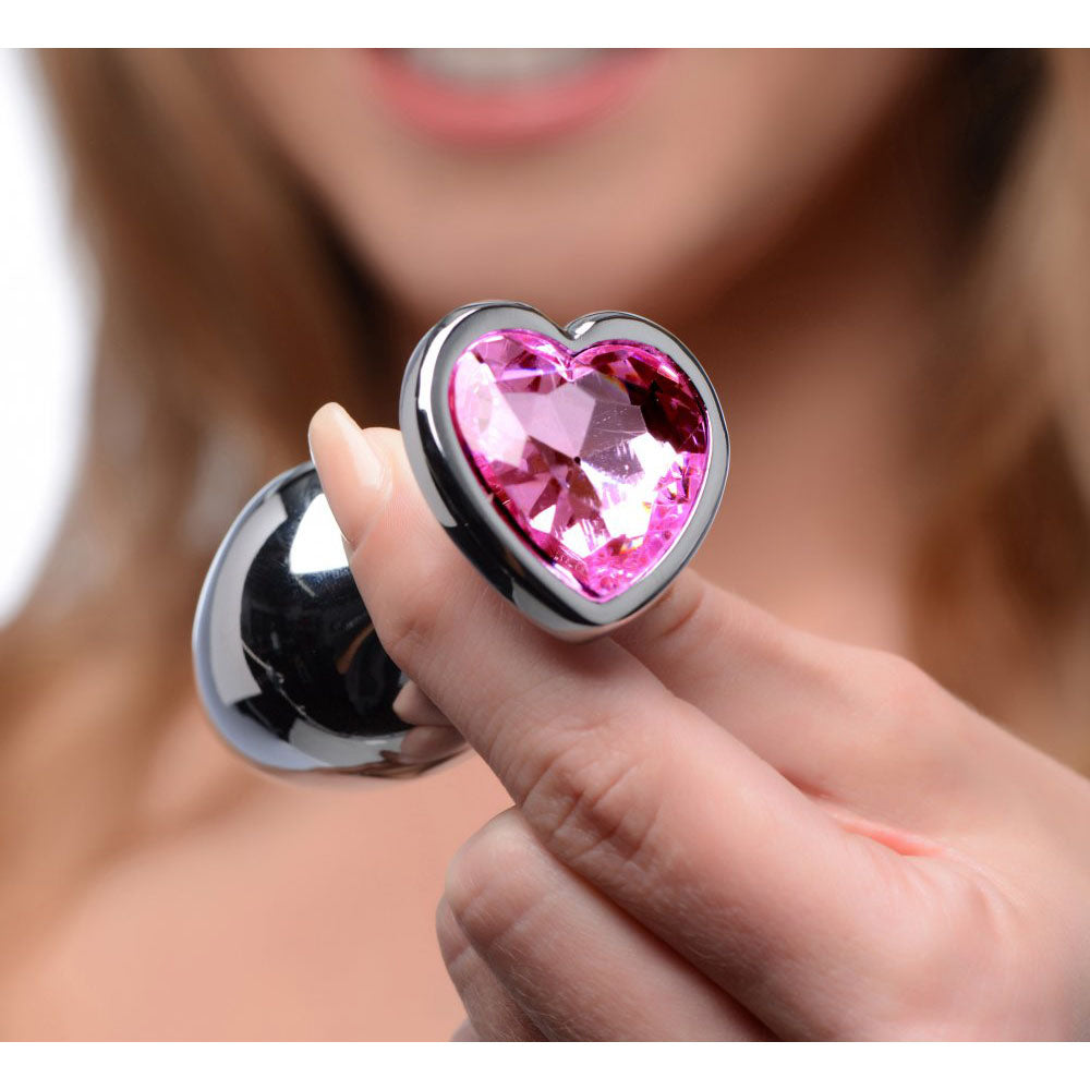 Model holding one plug from the Pink Heart Gem Teardrop Metal Butt Plug Training Set, with its pink heart facing forward for scale.