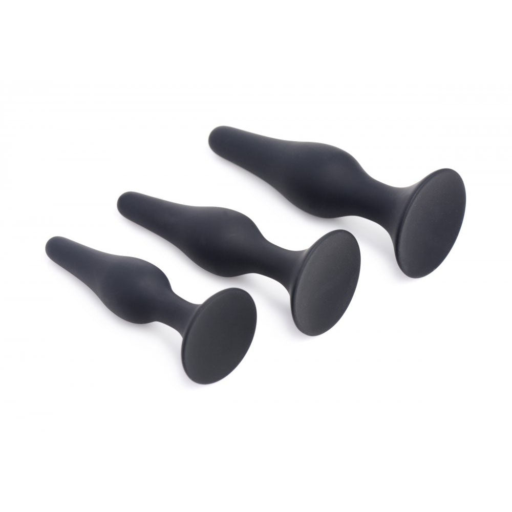 Three graduated black plugs from the Tapered Silicone Suction Anal Training Set angled to show their long profiles and round bases.