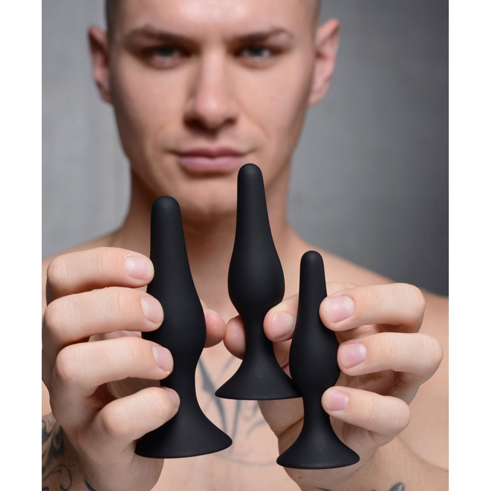Model holding the Tapered Silicone Suction Butt Plug Training Set with both hands to show the 3 sizes.