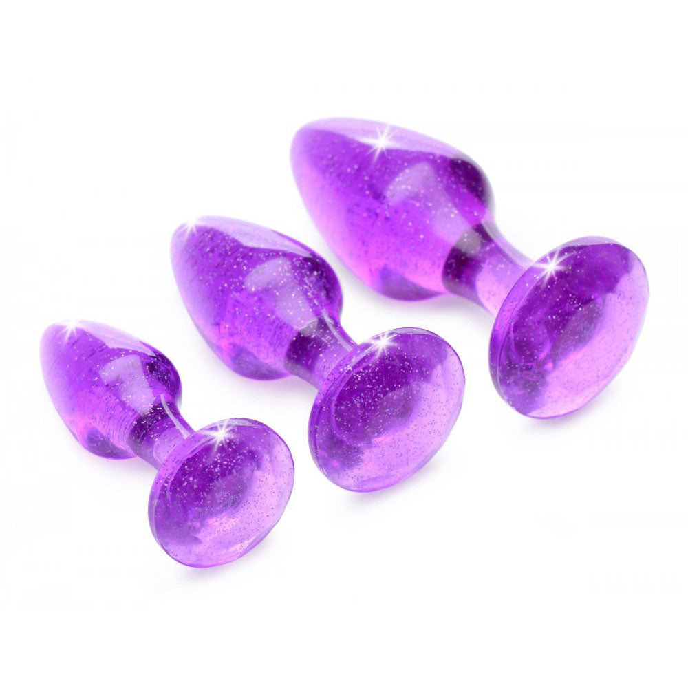 Three purple glitter anal plugs angled on their sides with rounded tips and flared bases.