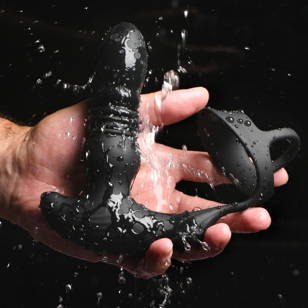 Black silicone thrusting plug with cock and ball ring rinsed under running water in a hand.
